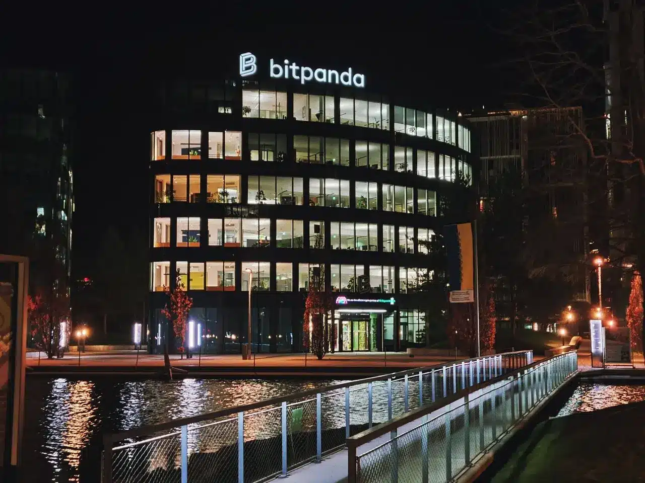 Night view of the Bitpanda office building with illuminated signage and glass facade near a canal.