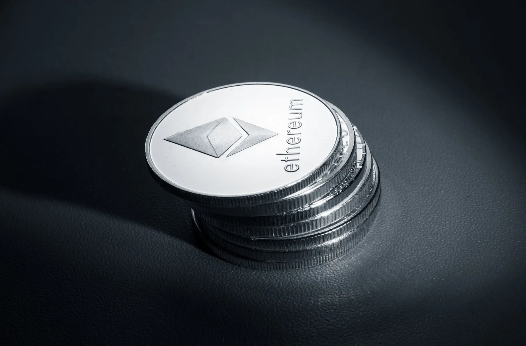 A stack of physical silver-colored Ethereum coins with the diamond logo and 'ethereum' text on a dark surface.