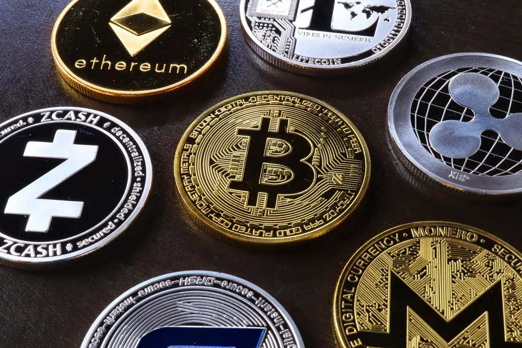 Physical cryptocurrency coins including Bitcoin, Ethereum, Zcash, Ripple, and Monero on a dark surface