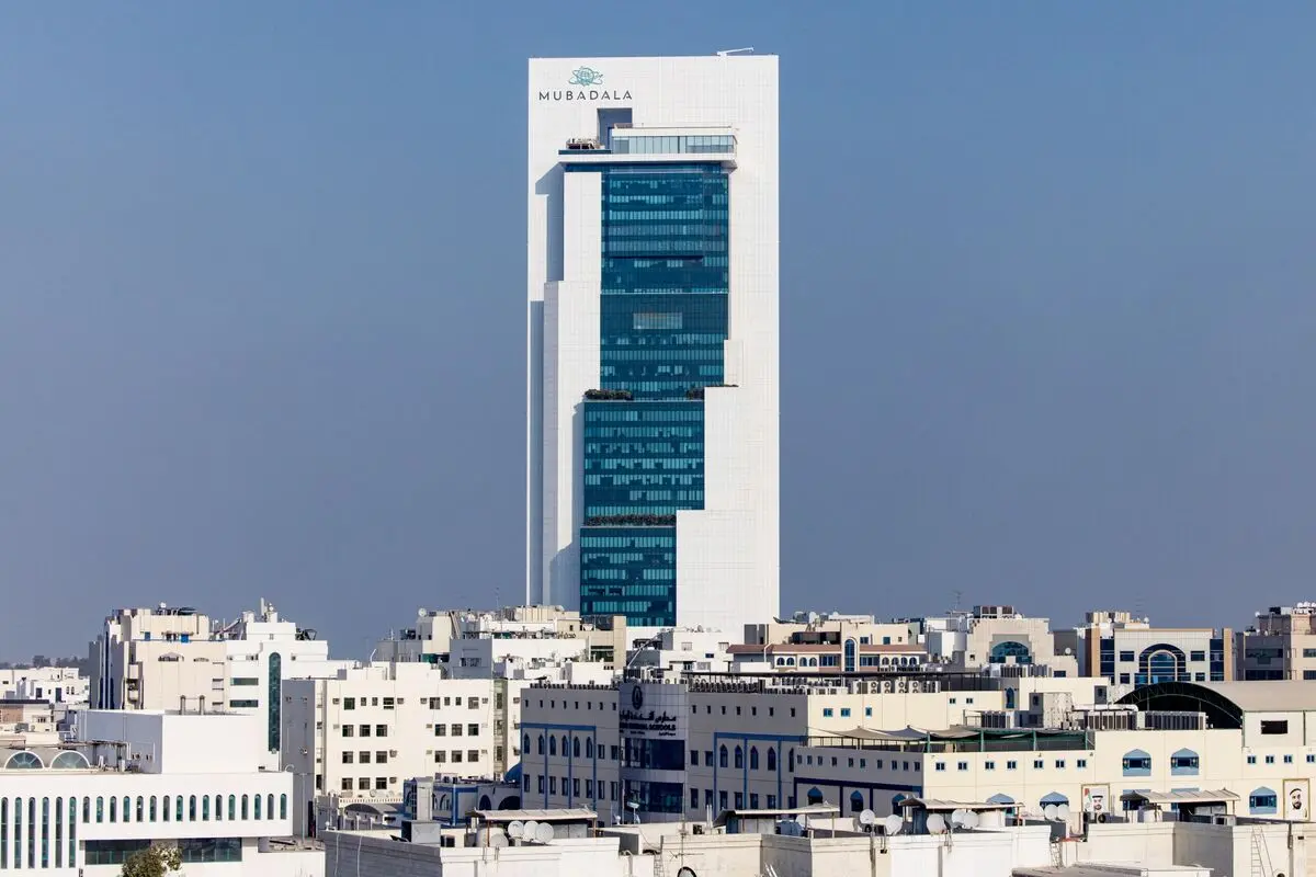 The white Mubadala headquarters skyscraper with blue glass windows overlooking the Abu Dhabi skyline.