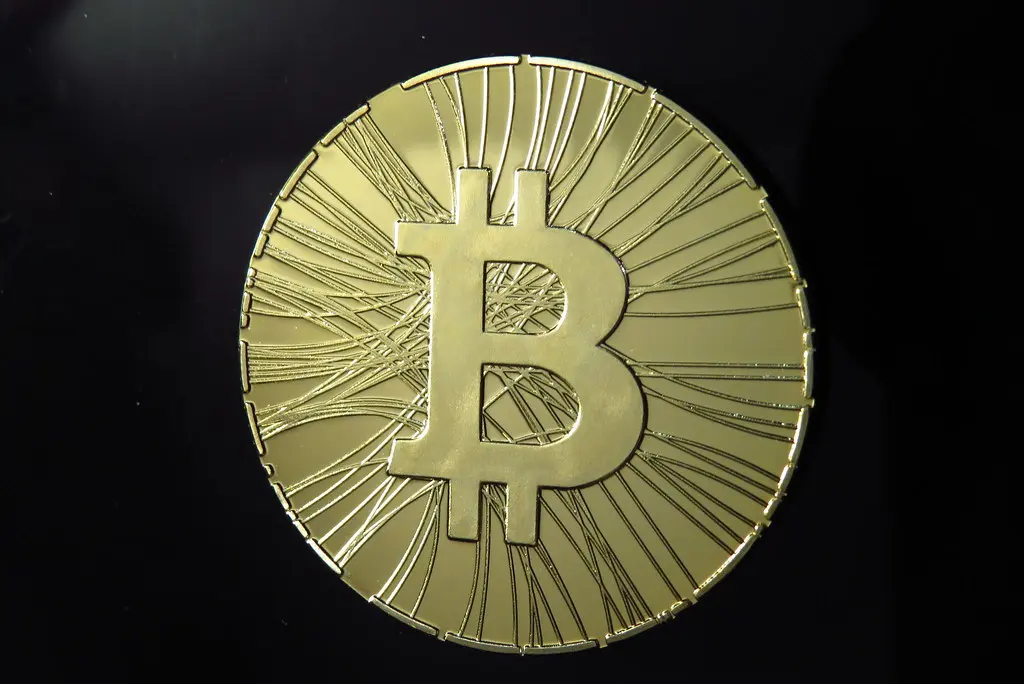 Eine goldfarbene physische Bitcoin-Münze vor schwarzem Hintergrund.