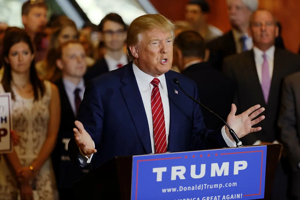 Donald Trump spricht an einem Rednerpult mit seinem Namen und dem Slogan „Make America Great Again“.