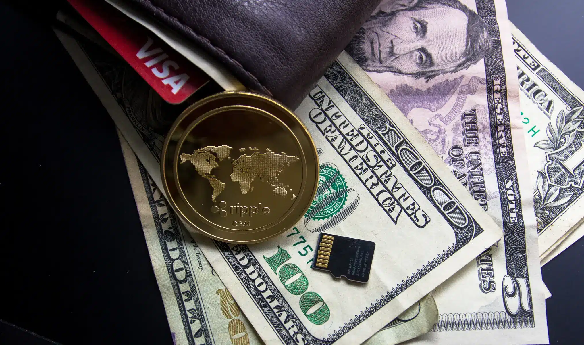 Eine goldene Ripple-XRP-Münze auf US-Dollar-Banknoten neben einem Portemonnaie und einer SD-Karte